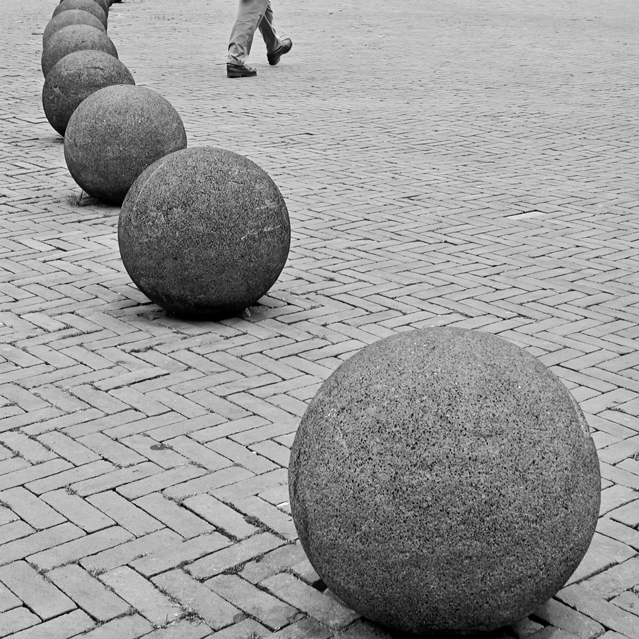 A row of large stone spheres on a brick-paved surface with a person walking in the background.