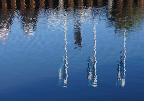 Reflections of flag masts and trees on calm water.