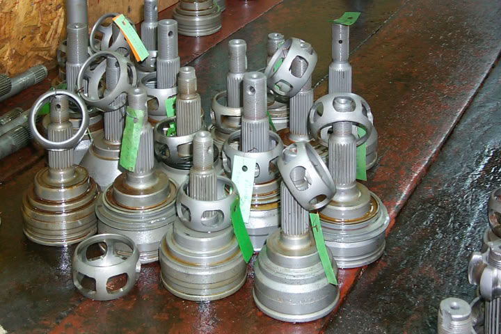 A collection of metal mechanical parts with cylindrical bases and vertical rods, some with green tags, placed on a wooden surface.