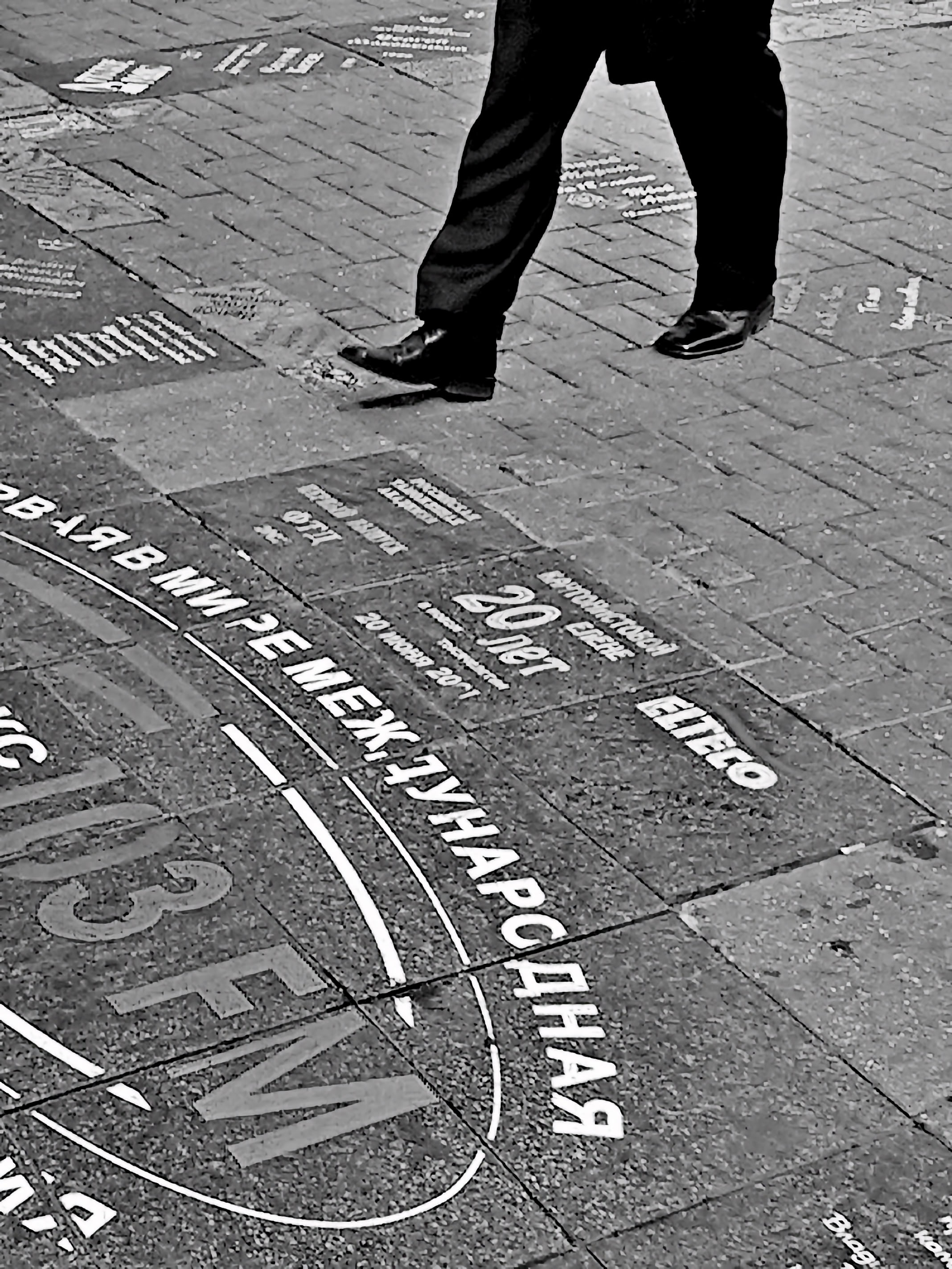 A person walking on a cobblestone street with various text and numbers painted on the ground in Moscow.