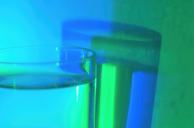 A glass of water with a blue and green light reflection on the surface and background.