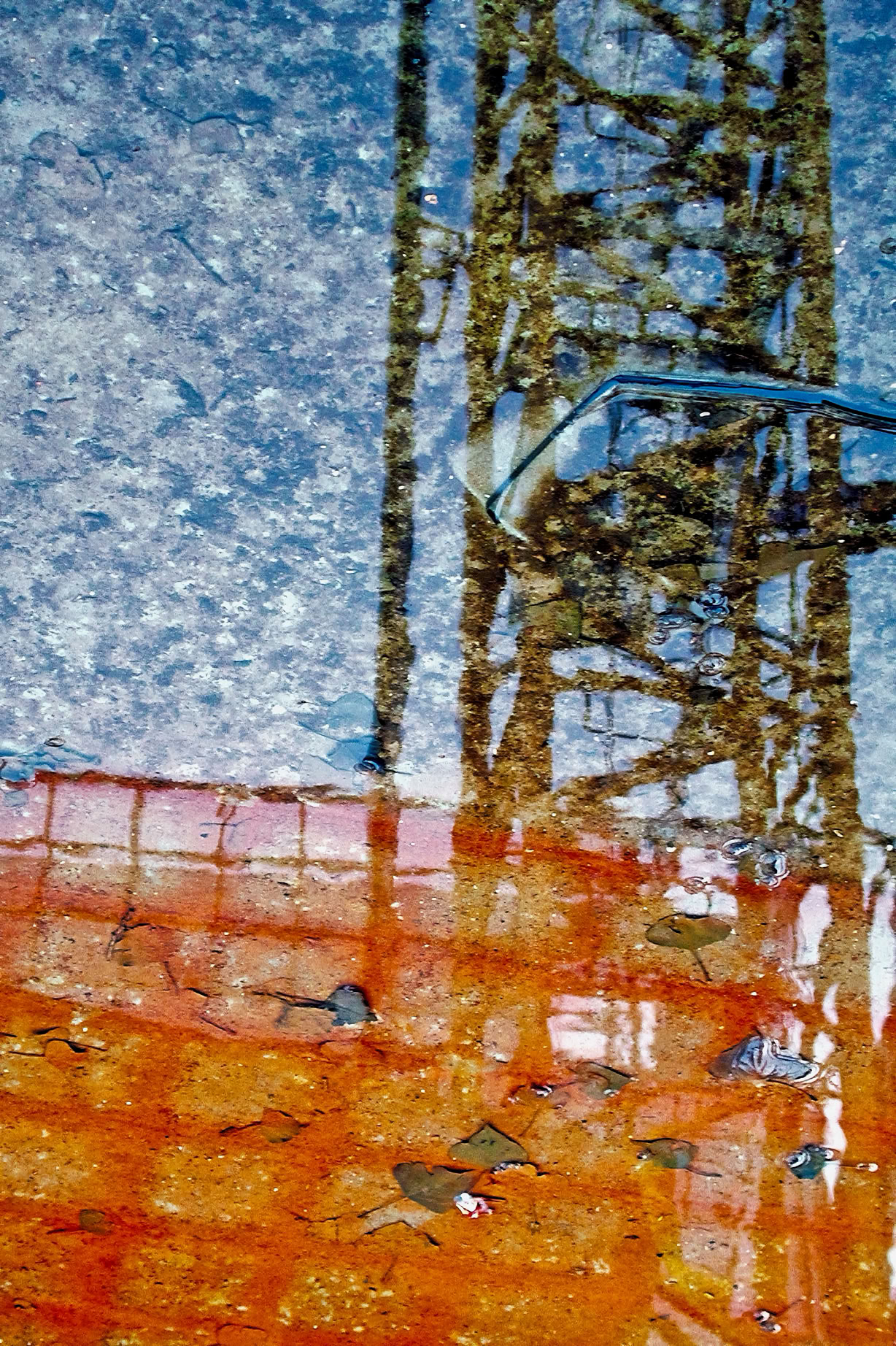 Reflection of a construction crane and orange netting in a puddle.